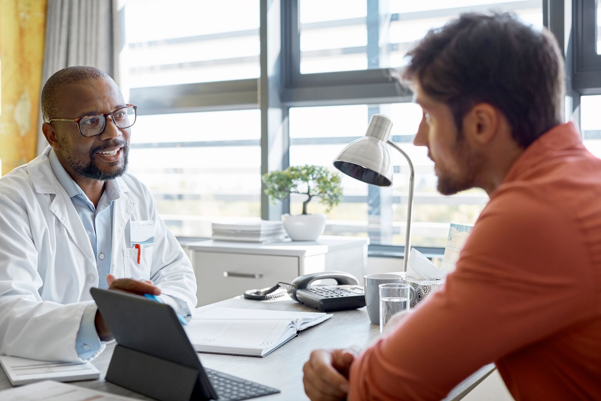 A doctor is sitting at a desk talking to a patient.