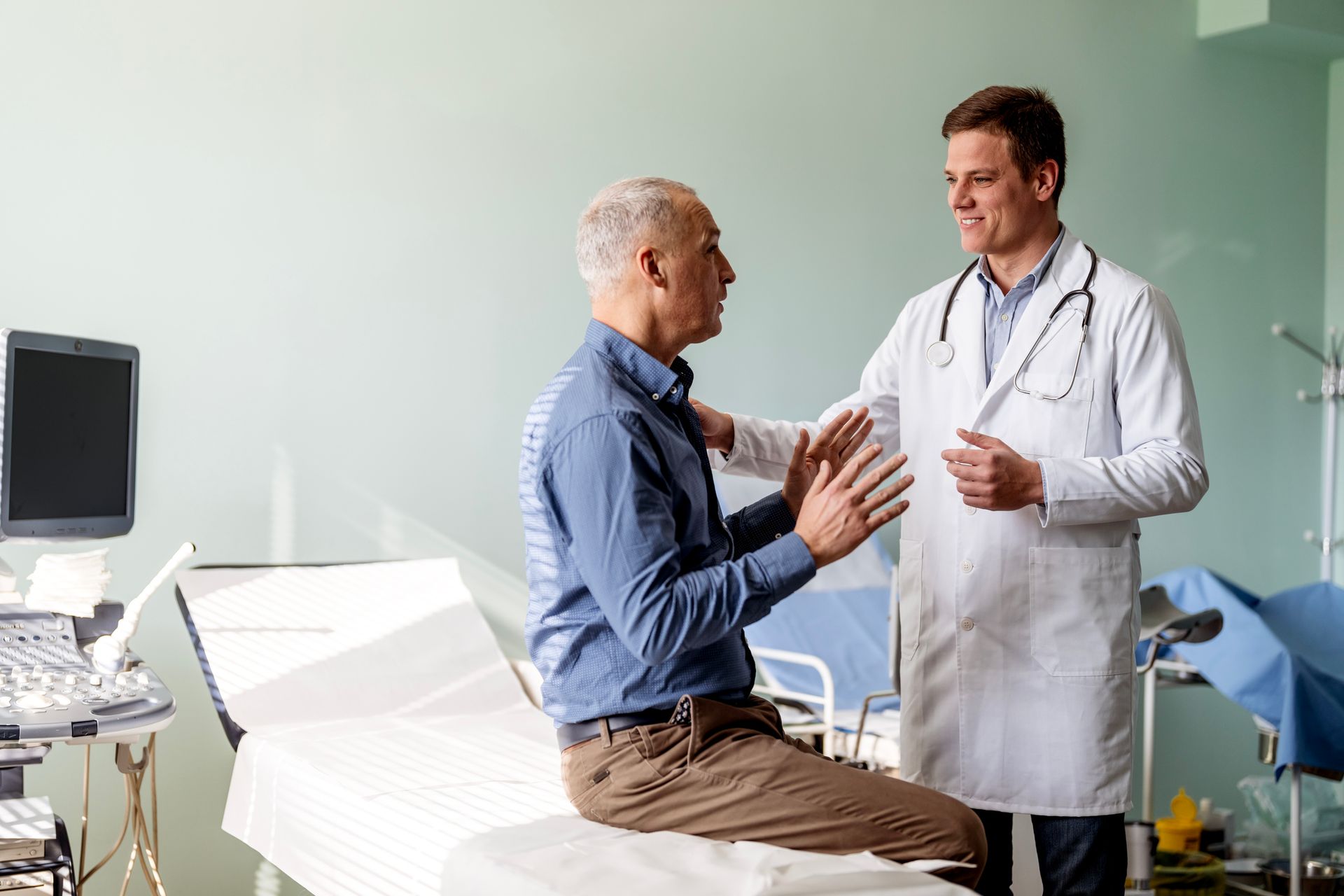 A doctor is talking to a patient who is sitting on a hospital bed.