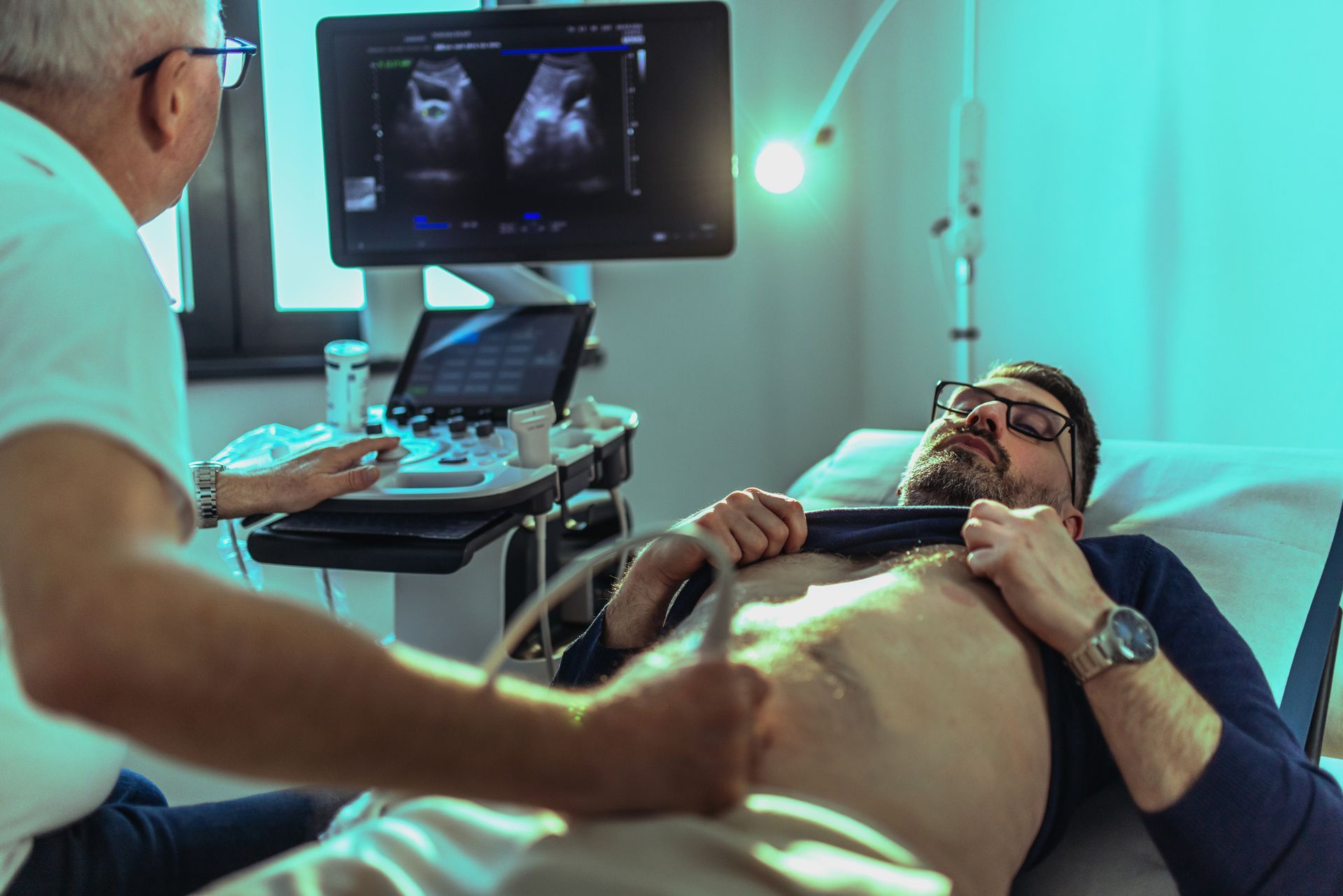 A man is laying in a hospital bed getting an ultrasound from a doctor.