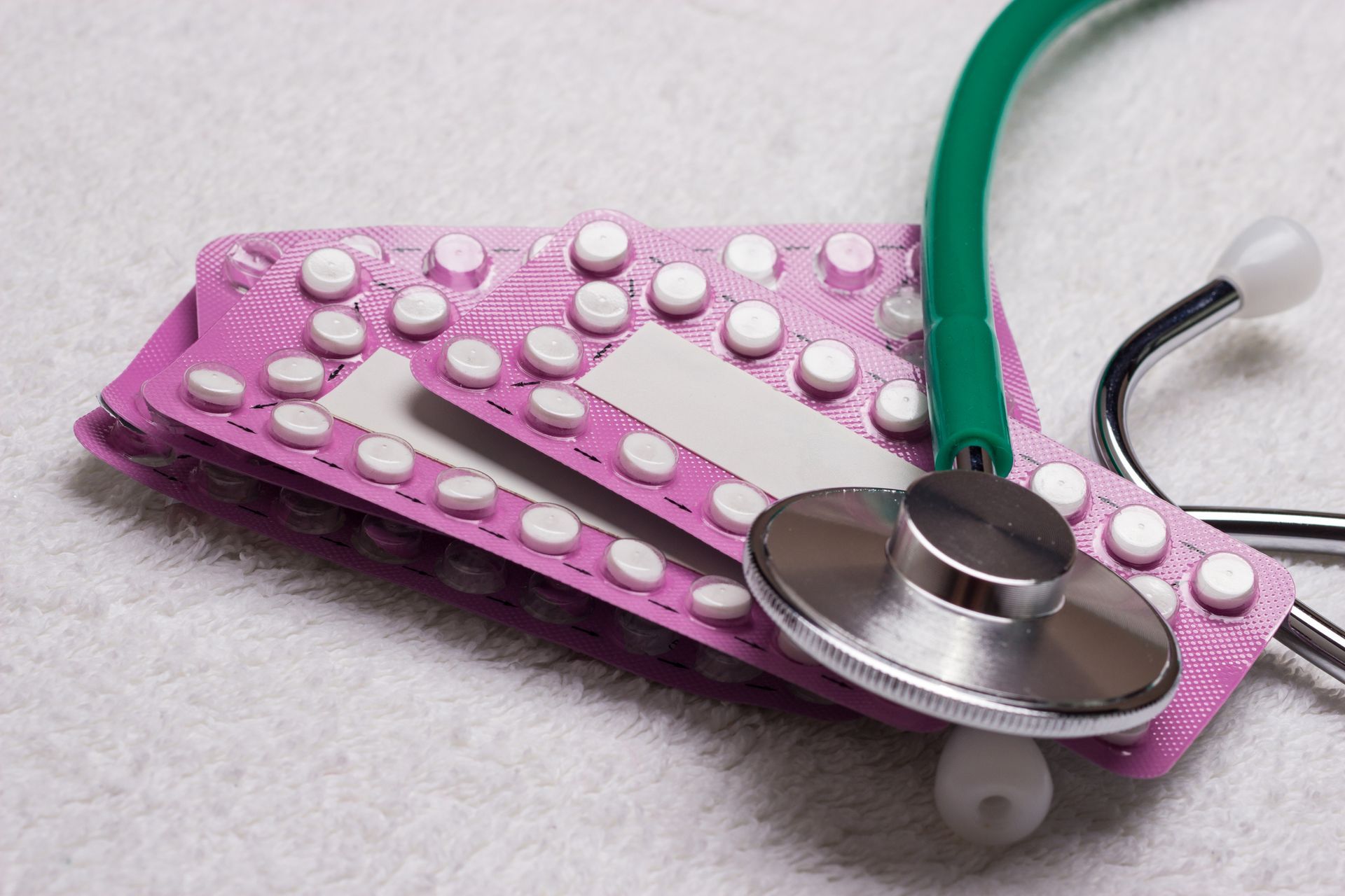 A stethoscope is laying on top of a pink pill pack