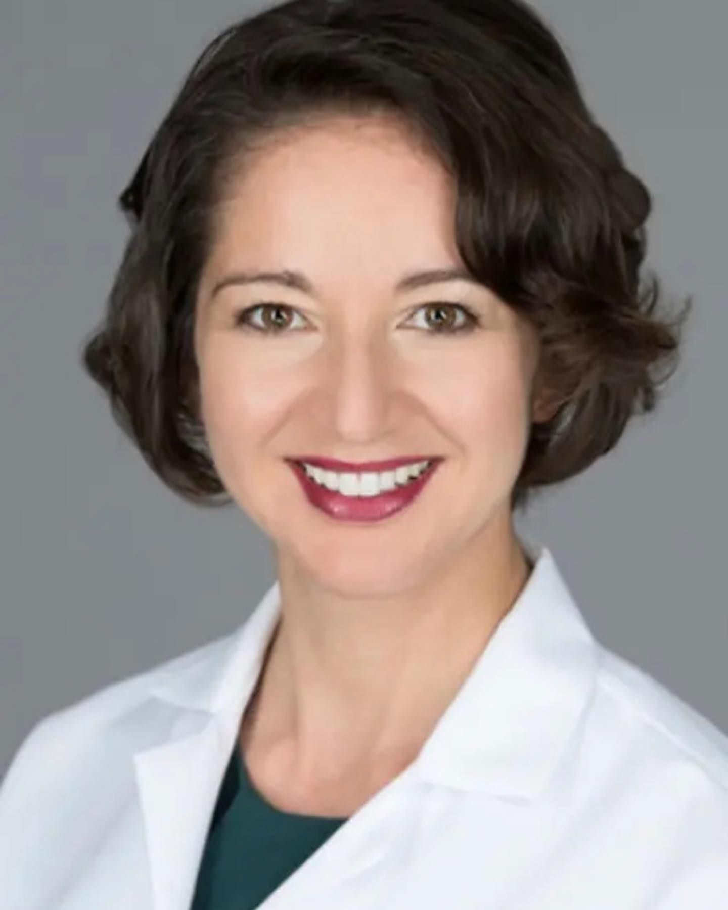 A woman in a white lab coat is smiling for the camera.