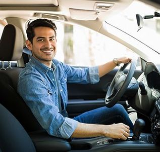 Smiling driver sitting in a car, holding the steering wheel and looking at the camera