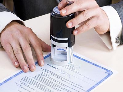 Hands stamping a document with a black approval stamp on a desk