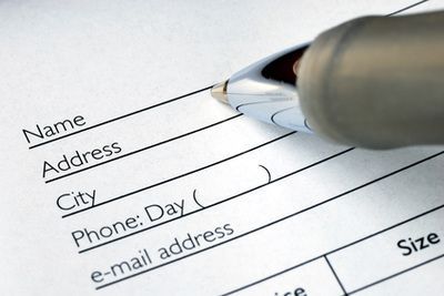 Pen filling out a paper form with fields for name, address, city, phone, and email