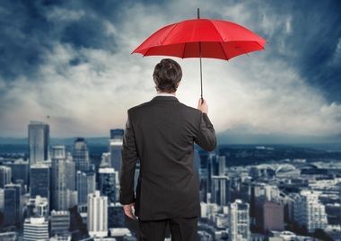 Man in a suit holding a red umbrella above a city skyline under cloudy skies