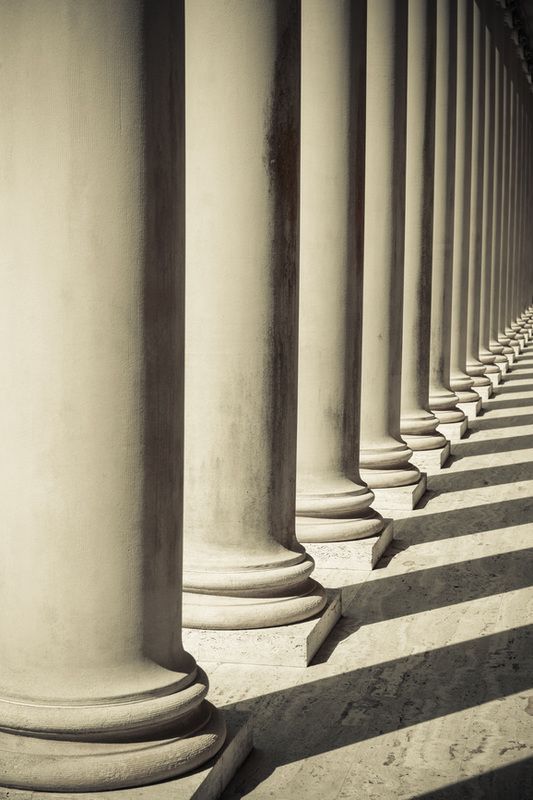 Row of tall stone columns casting long shadows in bright sunlight