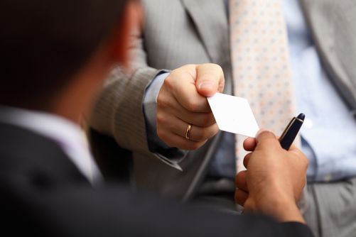 Hands exchanging a business card, with one person holding a pen in a meeting setting