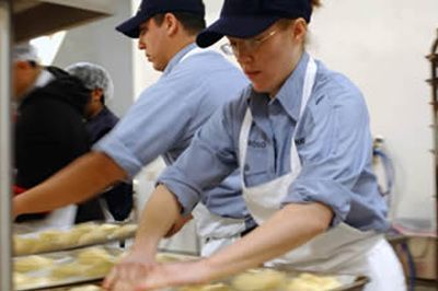 Workers in blue uniforms and aprons preparing food in a kitchen line