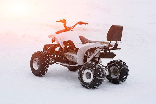 Snowy all-terrain quad bike with a backrest and orange flag parked in a white winter landscape