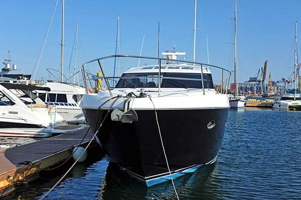Black-and-white motor yacht docked at a marina with other boats and blue water