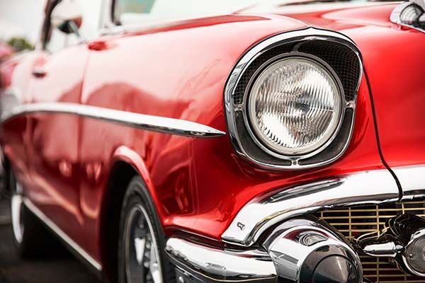 Close-up of a shiny red vintage car front with chrome headlight and grille