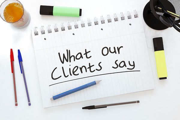 Notebook page reading “What our Clients say” with pens, a highlighter, and a coffee cup on a desk