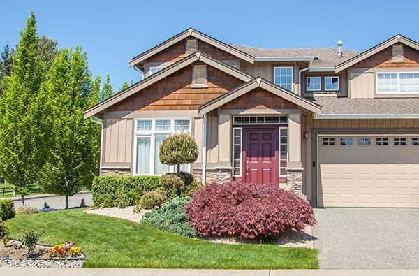 Suburban house with beige siding, red front door, two-car garage, and landscaped front yard