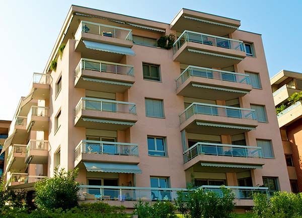 Pink apartment building with balconies and glass railings, seen from below against a blue sky