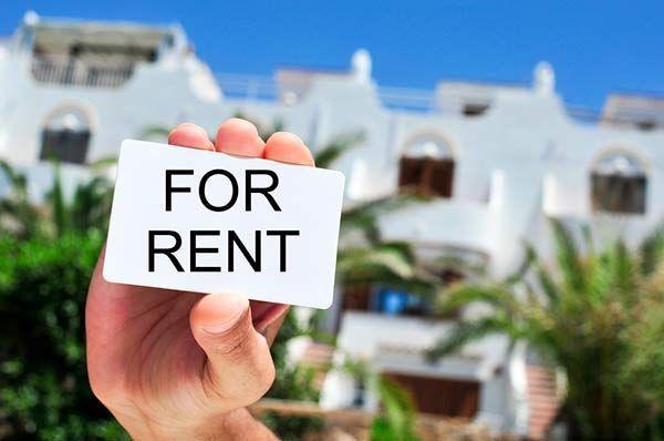Hand holding “FOR RENT” sign in front of a white building with balconies