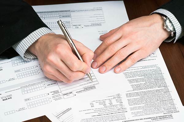 Hands signing a form on a desk with paperwork and pen.