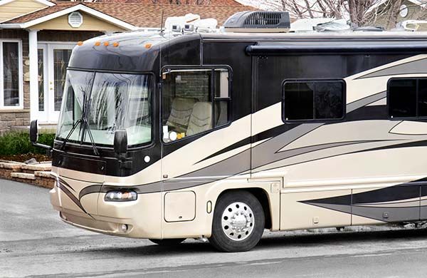 Beige and black motorhome parked in a driveway in front of a house.
