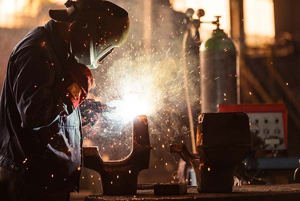 Welder in protective gear sparks metal in a dim workshop.