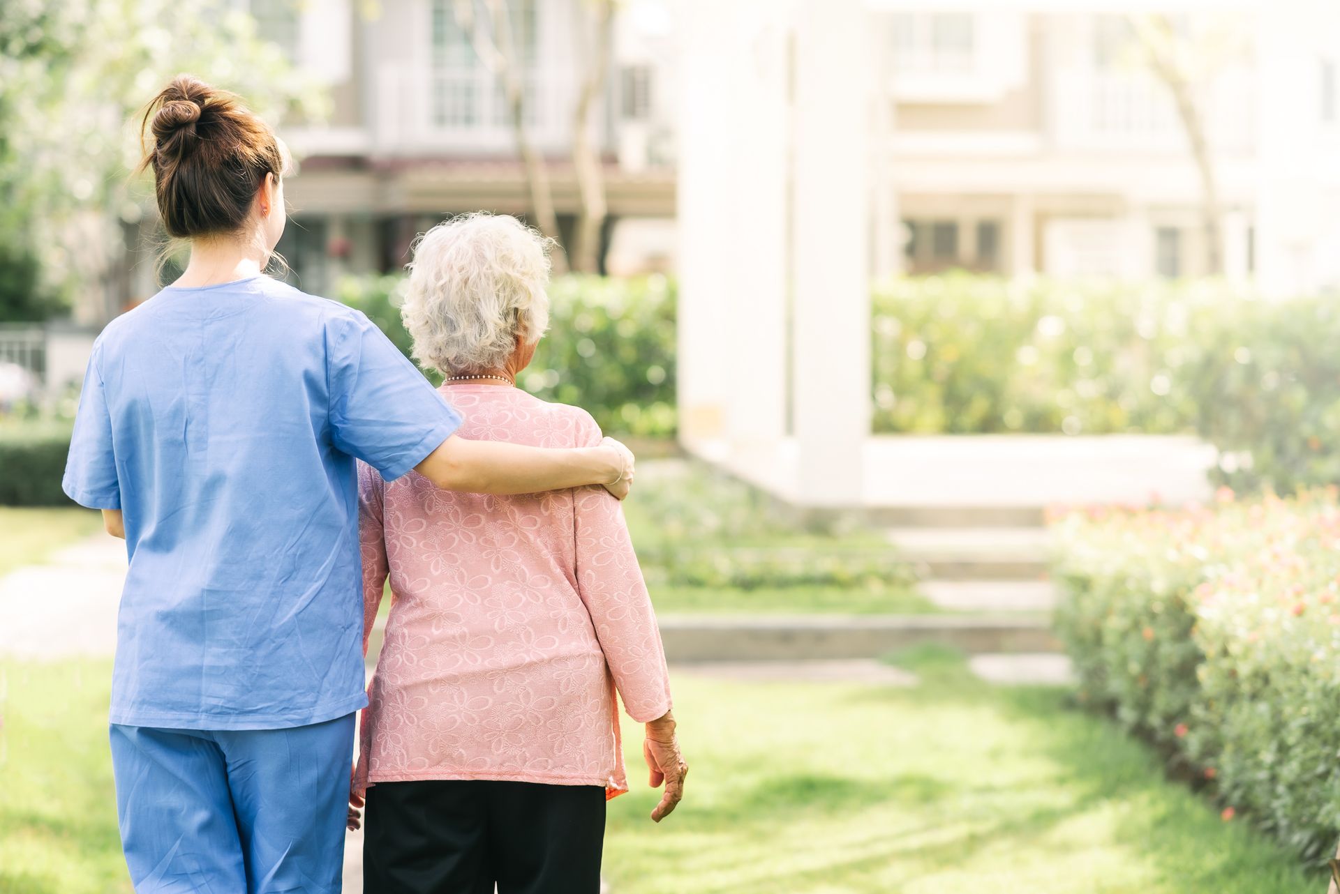 Two people walking arm in arm along a sunny garden path near a building Two people walking arm in arm along a sunny garden path near a building