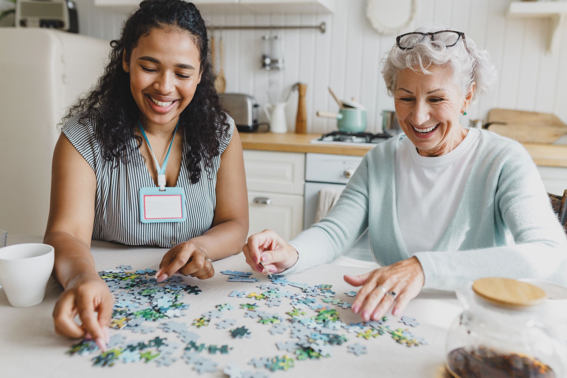 People eating together at a table in a bright dining room, chatting with a caregiver in the background People eating together at a table in a bright dining room, chatting with a caregiver in the background