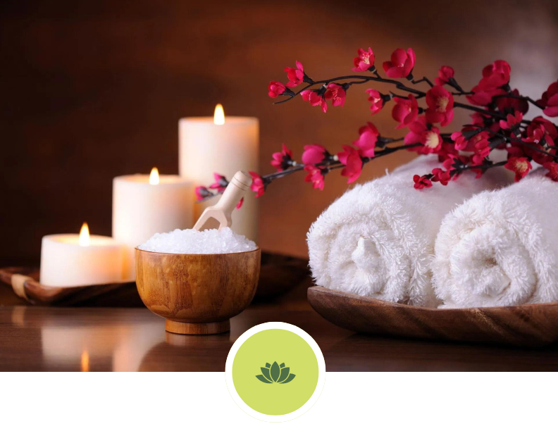 A bowl of salt sits on a table next to towels and candles.