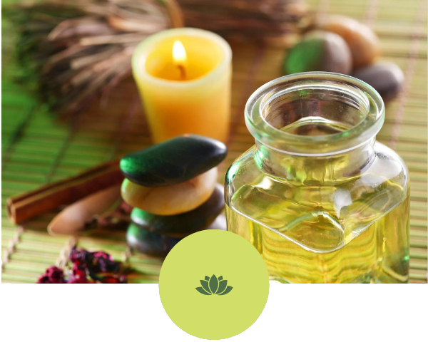 A bottle of oil is sitting on a table next to candles and rocks.