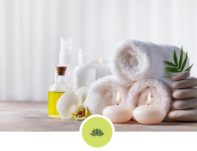 A stack of towels , candles , oil , flowers and rocks on a table.