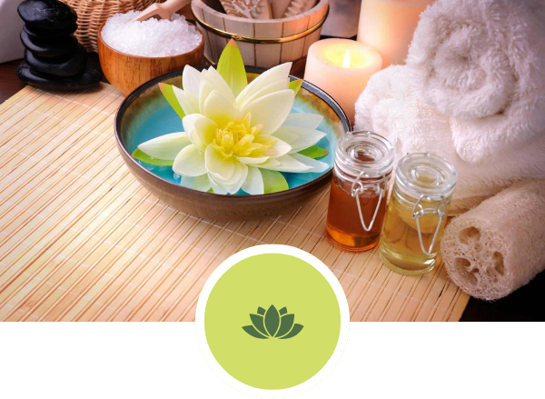 A lotus flower in a bowl next to candles and towels