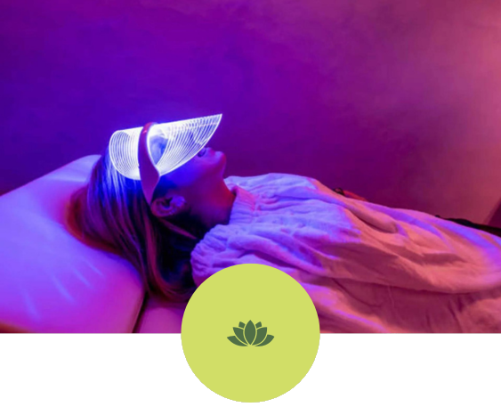 A woman is laying on a bed with a purple light on her face.