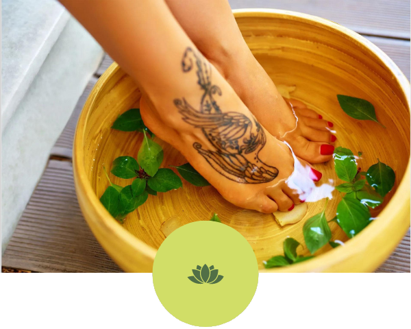 A woman with a tattoo on her foot is soaking her feet in a bowl of water.