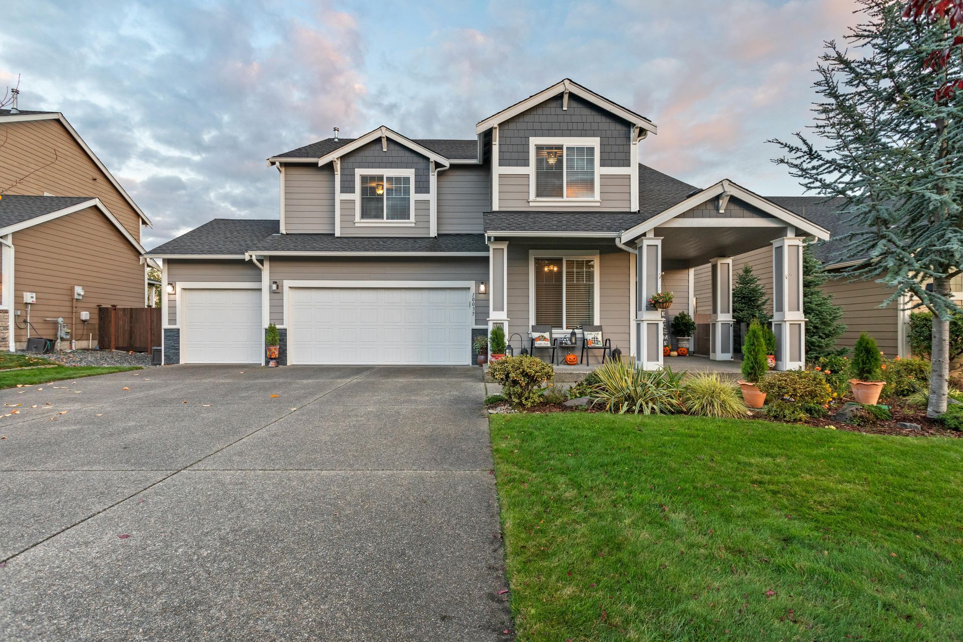 Two-story suburban house with gray siding, white garage, front porch, and landscaped lawn at dusk