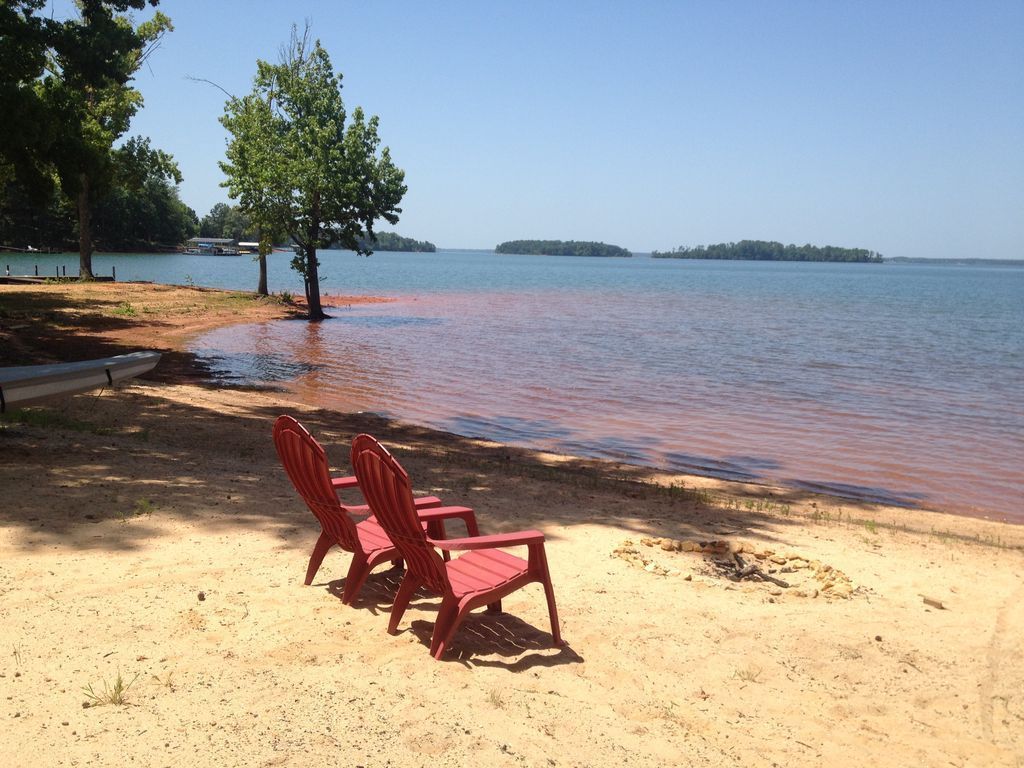 Two red chairs sit on a sandy beach near a body of water