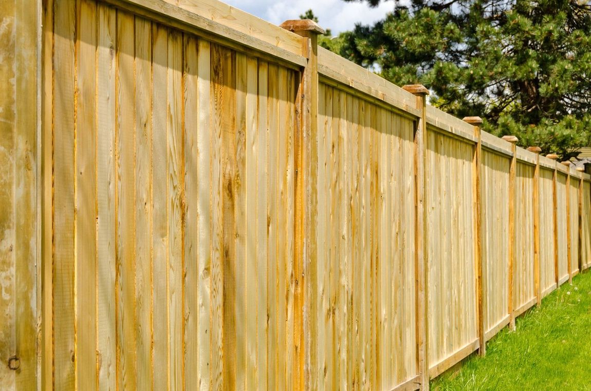 Wooden fence in a grassy yard, with vertical planks and decorative post tops.