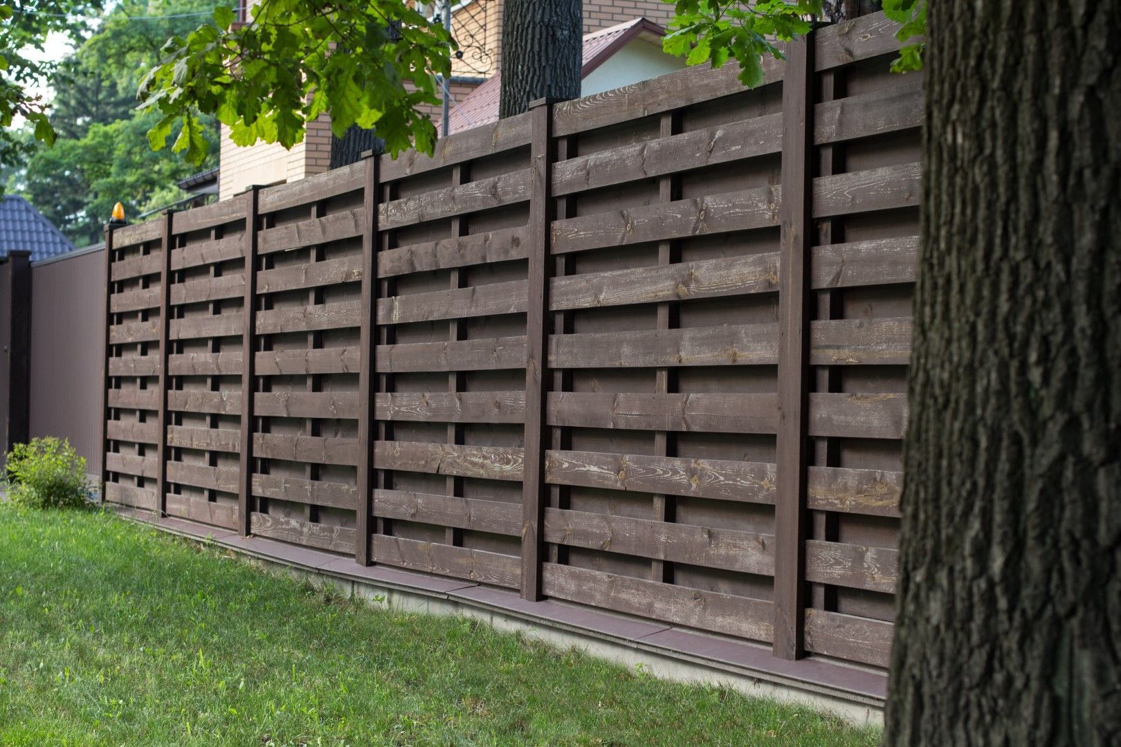 Brown wooden privacy fence in a grassy yard, with a tree in the foreground.