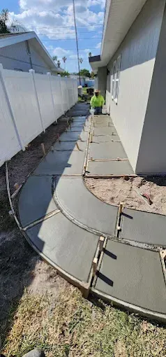 A walkway being constructed between a fence and a building. A worker is in the background.