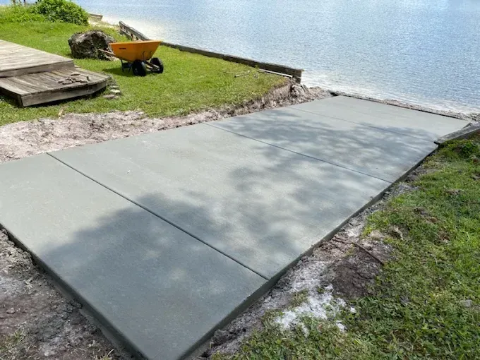 Newly poured concrete ramp leading to water, with grass, soil, and steps visible nearby.