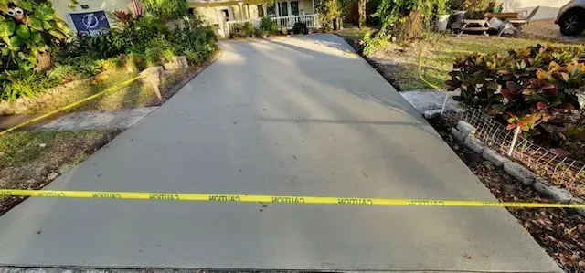 Newly poured concrete driveway, with yellow caution tape, leading to a house.