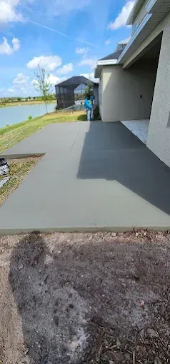 A concrete patio next to a house with a lake and blue sky in the background.