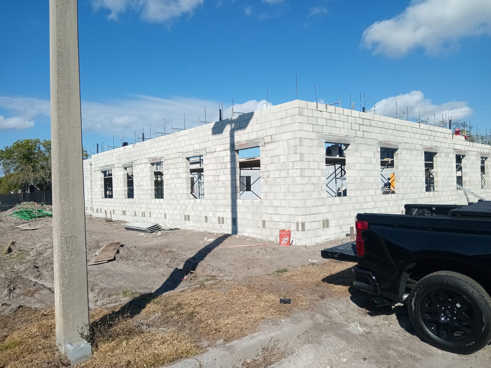 Construction of a one-story building with cinder block walls; black pickup truck parked beside it, bright sunny day.