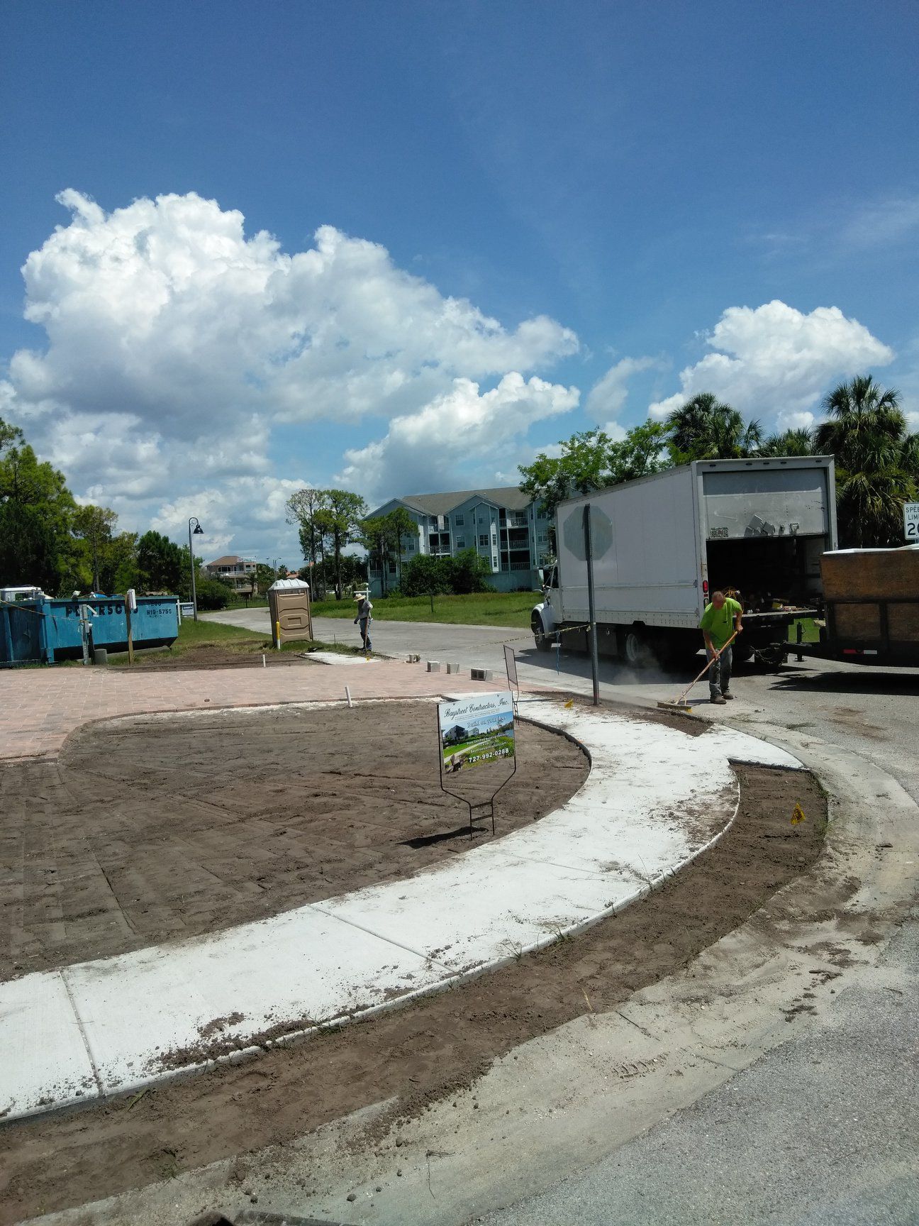 Workers landscaping around a concrete sidewalk with a truck, port-a-potties, and a clear blue sky with clouds. Workers landscaping around a concrete sidewalk with a truck, port-a-potties, and a clear blue sky with clouds.