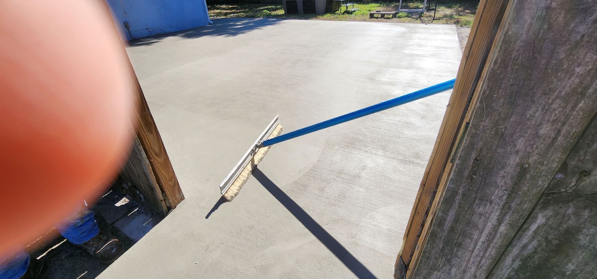 Finishing concrete surface being leveled with a long-handled tool, with a shadow cast on the surface. Finishing concrete surface being leveled with a long-handled tool, with a shadow cast on the surface.