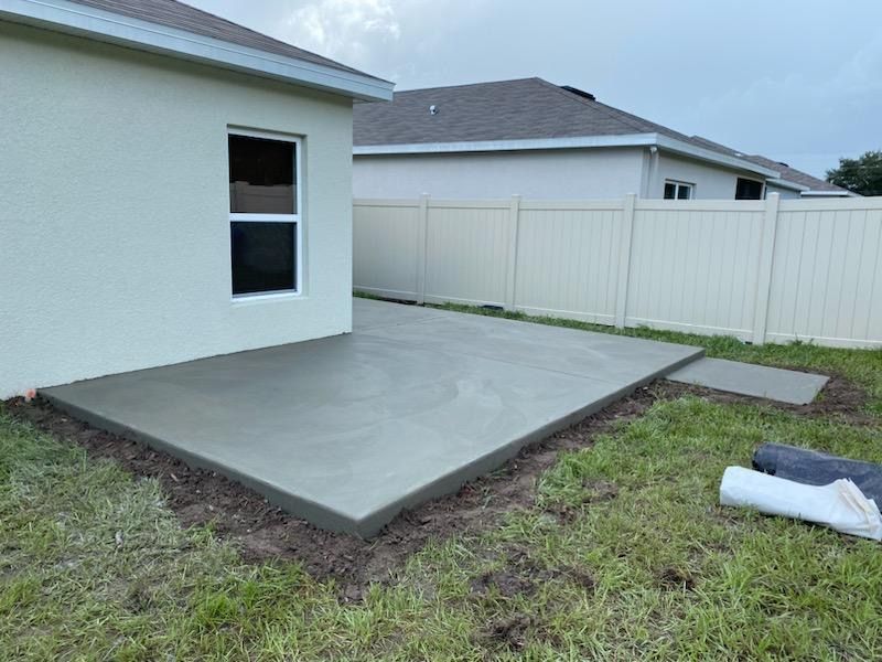 Newly poured concrete patio next to a house with a white fence and overcast sky. Newly poured concrete patio next to a house with a white fence and overcast sky.