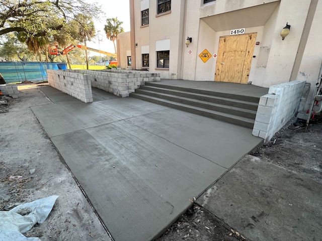 Freshly poured concrete ramp and steps leading to a building entrance. Construction ongoing.