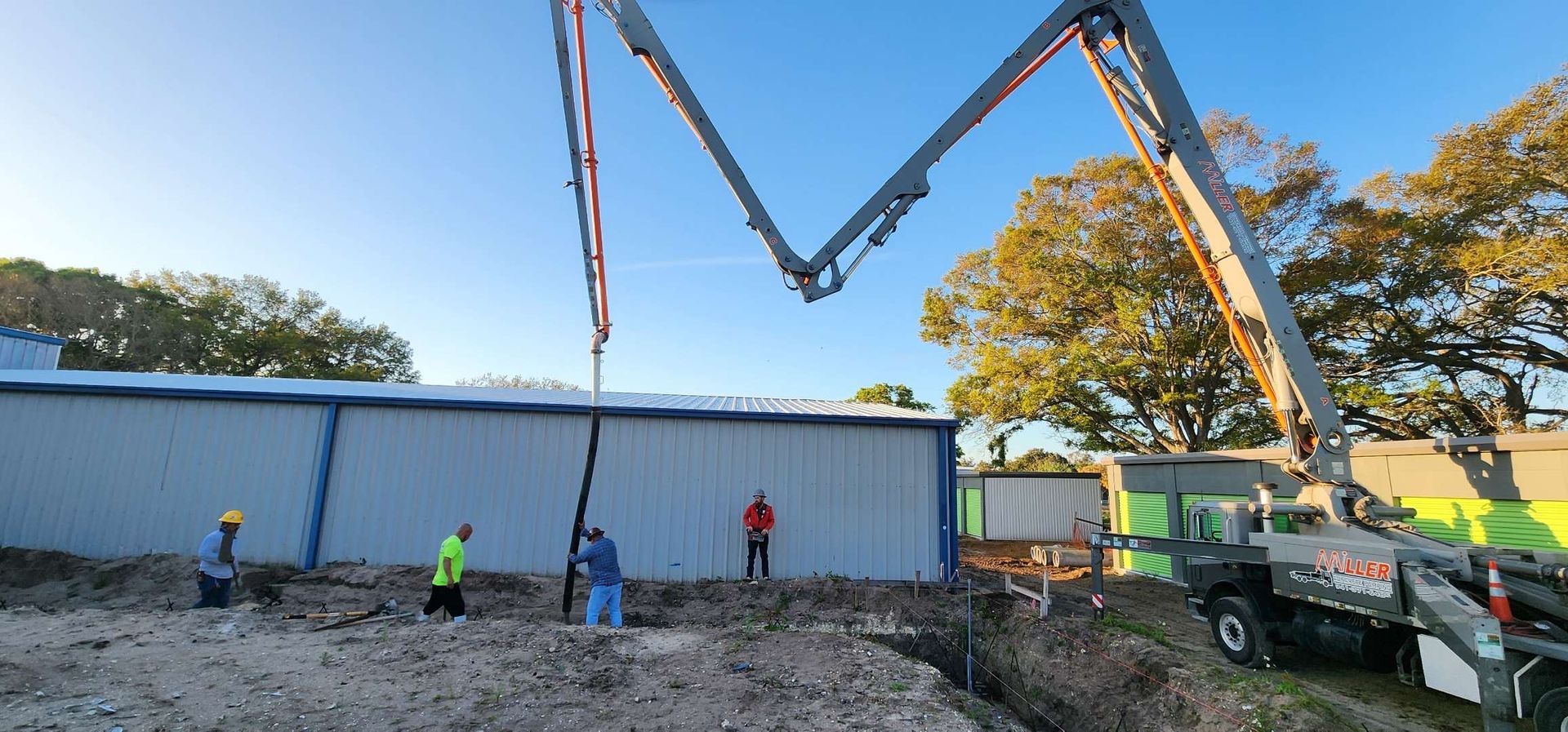 Concrete pump truck pouring concrete into a trench near a building; workers supervise. Concrete pump truck pouring concrete into a trench near a building; workers supervise.