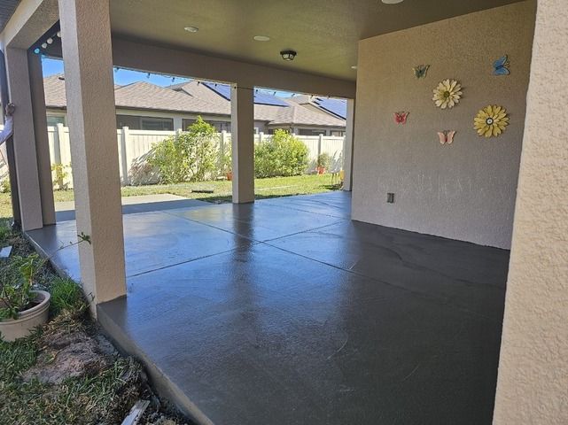 Covered patio with gray concrete floor, open to a backyard. Decorative flowers on wall.
