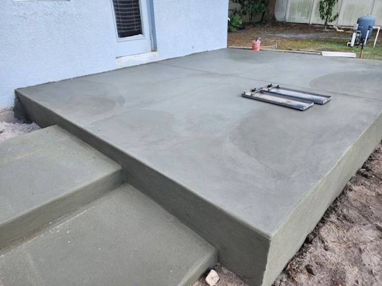 Newly poured gray concrete patio with steps in a backyard.