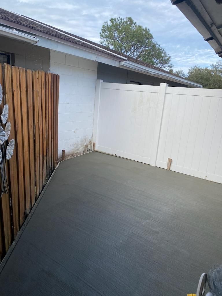 Freshly poured concrete patio next to a wooden fence and white vinyl fence, under a cloudy sky. Freshly poured concrete patio next to a wooden fence and white vinyl fence, under a cloudy sky.
