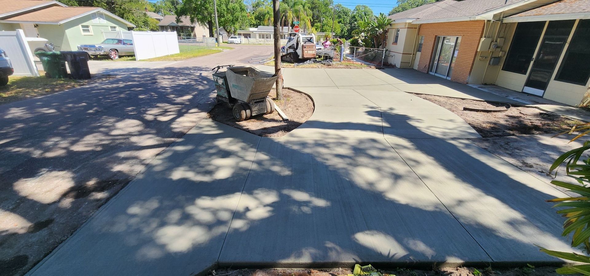 Concrete driveway and yard with shadows from tree. House in background.
