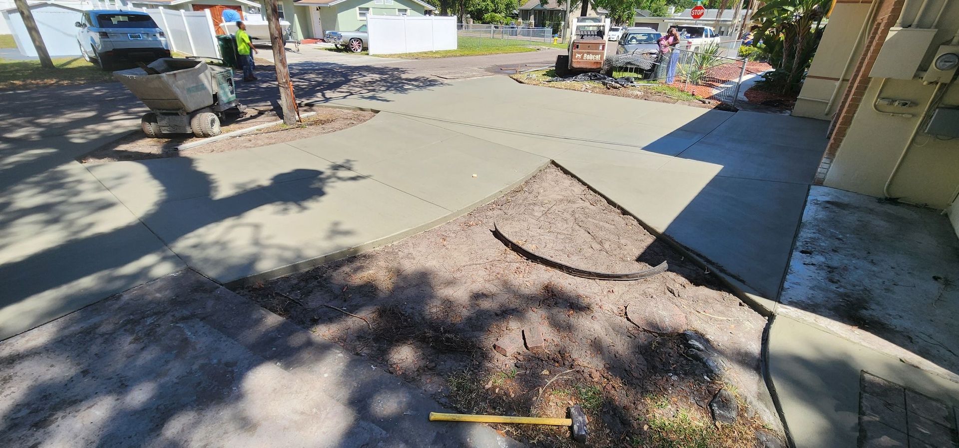 Workers pouring concrete on a driveway, with construction equipment and a partially paved area.