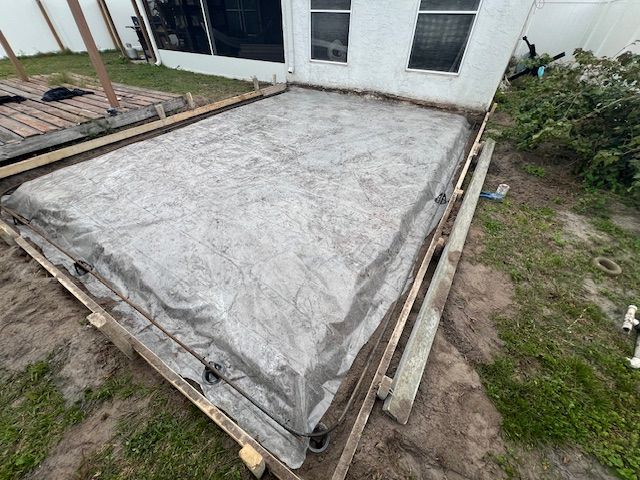 Concrete slab covered with tarp, framed by wooden boards, in a backyard setting. Concrete slab covered with tarp, framed by wooden boards, in a backyard setting.